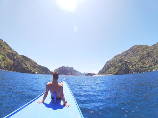 Calum sit on the bow of a boat which passes through a lagoon