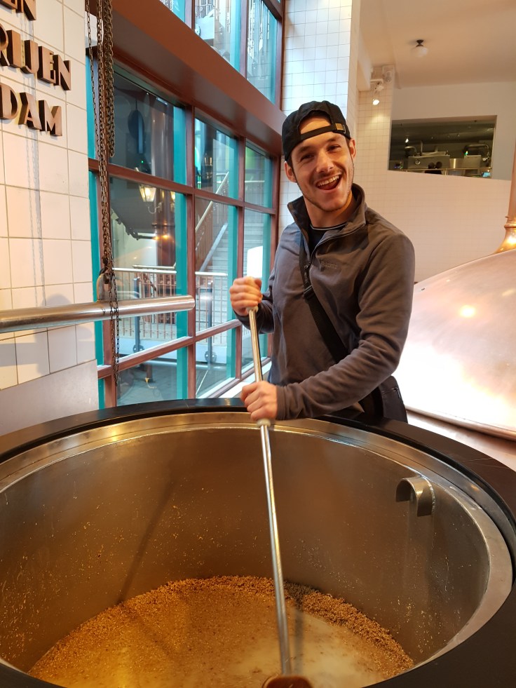 Person uses large spatula to mix hops in a vat